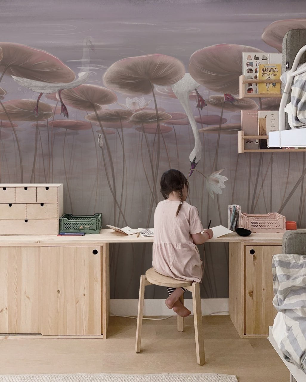 Child sitting at a desk in a room with a large wall mural of pink flamingos and lily pads.