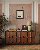 Wooden sideboard with decorative items against a wall with floral chinoiserie wallpaper